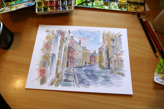 This is an original watercolour painting of South Bailey in Durham City, created in a contemporary urban sketching style. Strong ink lines and loose washes capture the historic street, colourful buildings, and the character of this iconic Durham location. signed j blakely