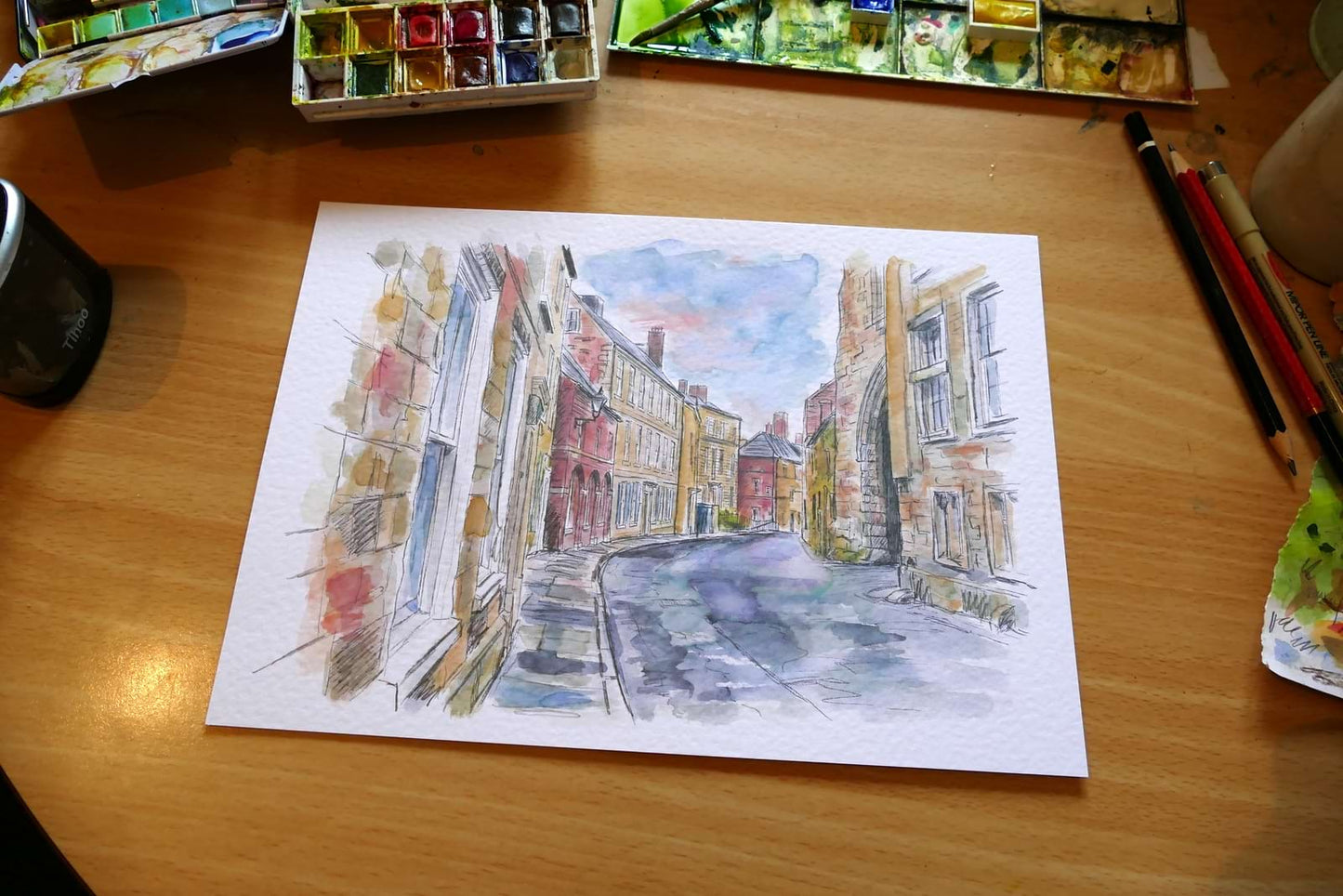 This is an original watercolour painting of South Bailey in Durham City, created in a contemporary urban sketching style. Strong ink lines and loose washes capture the historic street, colourful buildings, and the character of this iconic Durham location. signed j blakely